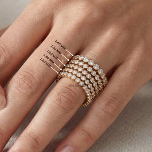Peut inclure: Une bague en or ornée d'une rangée continue de pierres rondes transparentes serties clos. L'image comporte des étiquettes indiquant des tailles de pierres de 1,60 mm, 1,80 mm, 2,00 mm, 2,20 mm et 2,40 mm, montrant les diamètres variables.