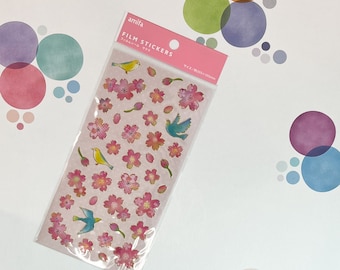 Pode incluir: Uma folha de adesivos de filme rosa com flores de cerejeira, pássaros e botões. Os adesivos são embalados em um saco de plástico transparente com o texto "amifa FILM STICKERS" e "サイズ:80x100mm".