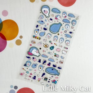 Puede incluir: Hoja de pegatinas transparente con ilustraciones de tem&aacute;tica marina. Las pegatinas representan ballenas, gatos y otras criaturas marinas en tonos azules, rosas y blancos. El texto "Little Milky Cat" est&aacute; impreso en la parte inferior.