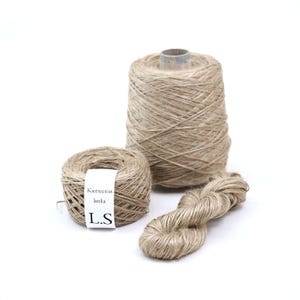 Peut inclure: Trois bobines de fil de lin naturel. Le fil est de couleur beige clair et est enroulé en forme de boule. Le fil est étiqueté "Kierteetoin lanka L.S."