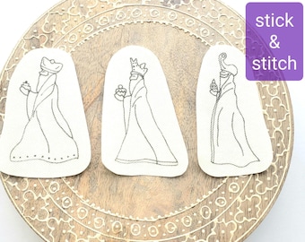 Può includere: Tre toppe ricamate raffiguranti i Re Magi, ognuno con un dono. Sono su uno sfondo chiaro, su un vassoio di legno decorativo. Il testo "stick & stitch" è in un rettangolo viola.