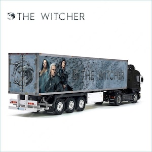 May include: A black semi-trailer truck with a white trailer. The trailer is decorated with a graphic of a wolf and the words "The Witcher".