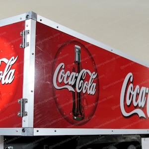 Pode incluir: Um caminhão de entrega Coca-Cola vermelho com o logotipo da Coca-Cola no lado. O caminhão é feito de metal e tem uma guarnição prateada. O caminhão é um modelo.