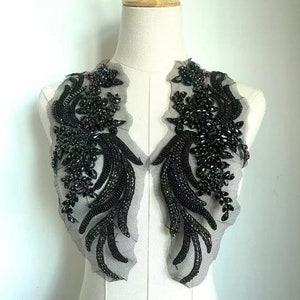 May include: A black beaded applique with a floral design. The applique features clusters of black beads and sequins, with a delicate net backing. The design is symmetrical, with two mirrored floral patterns. This decorative applique is suitable for embellishing garments.