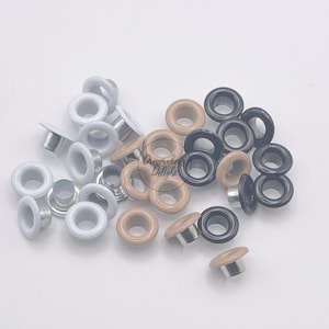 May include: A collection of metal eyelets in white, black, and brown. The eyelets are used for crafts and sewing projects.