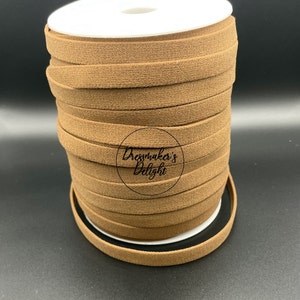 May include: A spool of brown, flat, textured ribbon. The ribbon is tightly wound on a white spool. The text "Dressmaker's Delight" is printed on the ribbon. The background is a dark gray.