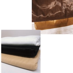 Puede incluir: Cuatro piezas de tela apiladas una encima de la otra. La pieza superior es blanca, la segunda es negra, la tercera es beige y la inferior es marrón.