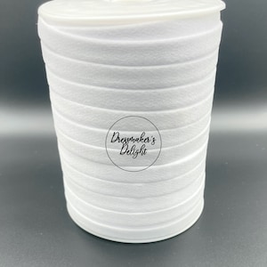 May include: A roll of white felt ribbon, tightly wound and stacked. The ribbon is a solid, bright white color. The image includes a circular logo with the text "Dressmaker's Delight". The ribbon is likely used for crafting and sewing projects.