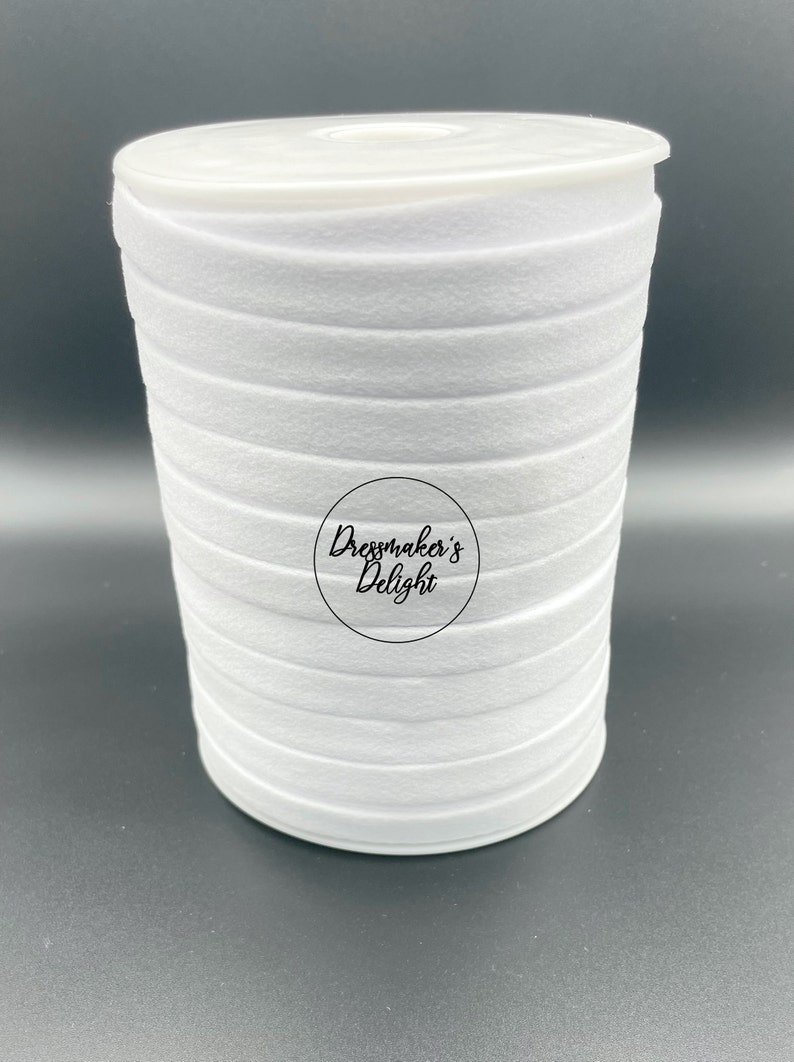 May include: A roll of white felt ribbon, tightly wound and stacked. The ribbon is a solid, bright white color. The image includes a circular logo with the text "Dressmaker's Delight". The ribbon is likely used for crafting and sewing projects.
