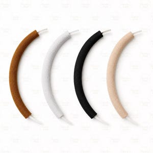 May include: Four curved, padded handles in brown, white, black, and beige. Each handle has a white plastic stem extending from one end. The handles are designed for a specific product, likely a bag or accessory.