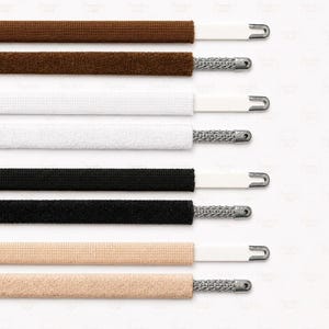 May include: Close-up of various shoelaces in brown, white, black, and beige. Each lace has a white plastic tip and a silver metal aglet. The laces are arranged horizontally against a white background.