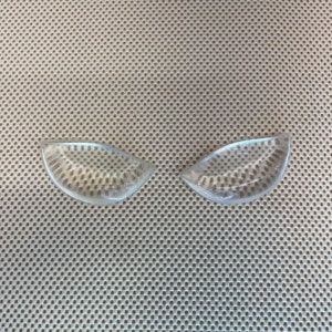 Puede incluir: Dos plantillas de gel transparentes, semicirculares, probablemente para zapatos, se muestran sobre un fondo de tela beige con lunares. Las plantillas tienen un patr&oacute;n texturizado de puntos dentro del gel transparente. El conjunto sugiere un enfoque en la comodidad y el soporte.