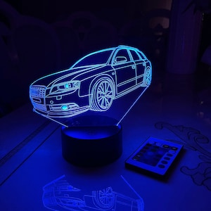以下が含まれることがあります： 車の形をした青い3Dプリントのナイトライト。ナイトライトは黒いベースに置かれ、リモコンが付いています。