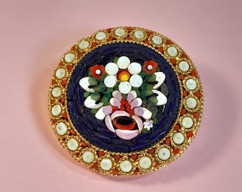 Vintage micro mosaic brooch with a white and pink flower set in a dark blue background.