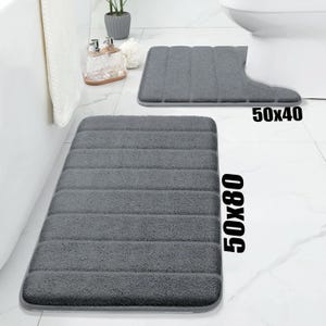 May include: Two grey bath mats. One is rectangular, measuring 50 x 80 inches (approx. 127 x 203 cm), and the other is shaped to fit around a toilet, measuring 50 x 40 inches (approx. 127 x 102 cm).