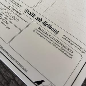 K&ouml;nnte beinhalten: Ein wei&szlig;er Papierplaner mit schwarzem Text und Illustrationen. Der Planer enth&auml;lt Abschnitte f&uuml;r "Gesundheit und Wohlbefinden" und "Andere Ermittlungen". Eine Spinne und eine Kr&auml;he sind im Design enthalten. Die Website creativelyhaunted.com ist unten aufgedruckt.