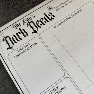 K&ouml;nnte beinhalten: Eine schwarz-wei&szlig;e Journalseite mit dem Titel "The Day's Dark Deeds". Die Seite enth&auml;lt Abschnitte f&uuml;r "Urgent Undertakings", "Order of Proceedings" und "Other Obligations". Ein Spinnennetz und eine Spinne sind Teil des Designs. Der Text "Recorded for posterity upon this date" ist ebenfalls vorhanden.
