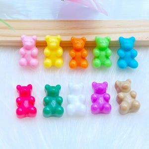 以下が含まれることがあります： ピンク、黄色、オレンジ、緑、青の10色のグミベア型のチャーム。下の段には赤、緑、白、紫、タンのクマが並んでいます。これらの小さなプラスチック製のチャームは、クラフトプロジェクトに最適です。