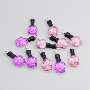 May include: Twelve nail polish bottle charms, six pink and six purple, with silver jump rings. The charms are made of glitter-filled plastic and have a black cap.