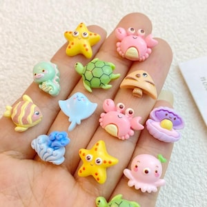Puede incluir: Una colección de figuras marinas en miniatura de colores, incluyendo estrellas de mar, cangrejos, tortugas y peces. Las figuras son de varios colores y tienen rasgos de dibujos animados.