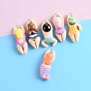 May include: A collection of six miniature figurines, each depicting a person in a swimsuit. The figurines have a cream-colored body and are adorned with various swimsuit designs, including polka dots, stripes, and a mermaid tail. Each figure has a silver loop at the top.