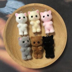 May include: Six plush cat charms in various colors, including white, pink, brown, black, and gray. Each charm has a loop for attaching to a keychain or bag.