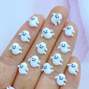 Puede incluir: Una colección de pequeños adornos blancos con forma de fantasma y caras sonrientes. Estos fantasmas en miniatura están dispersos sobre una superficie, mostrando su diseño simple y amigable. Ideal para manualidades o para agregar un toque espeluznante.