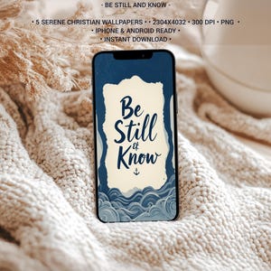 Könnte beinhalten: Ein Smartphone zeigt ein ruhiges christliches Hintergrundbild mit dem Text "Be Still & Know" in einem marineblauen und cremefarbenen Design. Das Telefon liegt auf einer gemütlichen, cremefarbenen Strickdecke, mit einer weißen Tasse und getrockneten Pflanzen im Hintergrund.