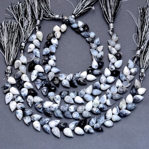 May include: A strand of black and white teardrop-shaped opal beads with a black and white speckled pattern. The beads are strung on a cord with tassels at each end.