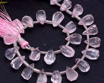 May include: A strand of pink rose quartz gemstone beads, each bead is faceted and shaped like a teardrop. The beads are strung on a silver wire and have a pink tassel at one end.