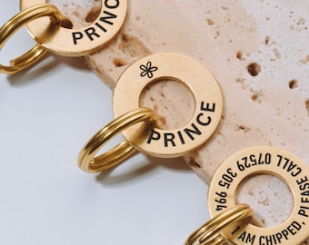 May include: Gold-colored pet ID tags with the name "PRINCE" in black lettering. Each tag has a small flower symbol and a split ring for attachment. One tag includes a phone number and the text "I AM CHIPPED. PLEASE CALL".