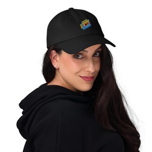 May include: Black baseball cap with a curved brim. The cap features a colorful embroidered design of a retro cassette tape on the front. The cap is made of a soft material and is suitable for everyday wear.