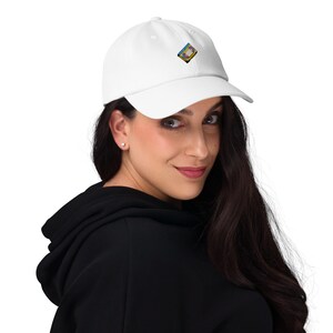 May include: White baseball cap with a small, colorful embroidered design on the front. The design appears to be a retro-style video cassette. The cap is made of a soft material and has a curved brim.