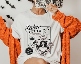 May include: White t-shirt with a black and white graphic design featuring a witch, books, and the text "Salem Book Club". The graphic also includes bats, a cauldron, a skull, and the text "All witches welcome".