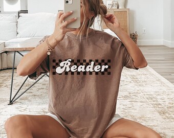 May include: A brown t-shirt with a white checkered pattern and the word "Reader" in a retro font.