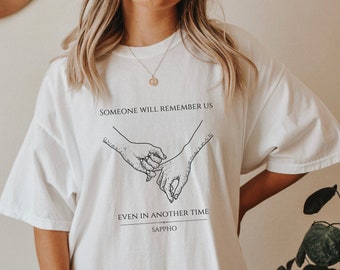 May include: White t-shirt with a black graphic of two hands holding each other. The text "Someone will remember us even in another time Sappho" is printed below the graphic.