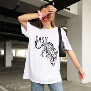 May include: White oversized t-shirt with a black and white tiger graphic and the word "EASY" printed on the front.
