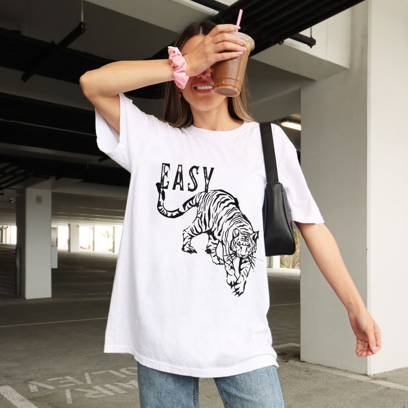May include: White oversized t-shirt with a black and white tiger graphic and the word "EASY" printed on the front.