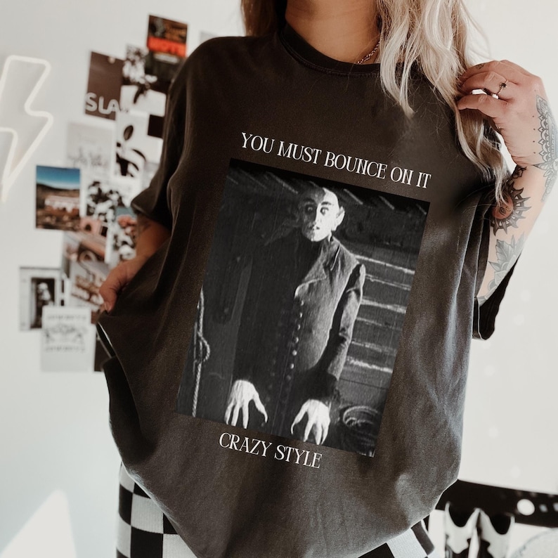 May include: A dark gray t-shirt with a black and white image of a man with a creepy expression. The text "You must bounce oh it" and "Crazy Style" are printed on the shirt.