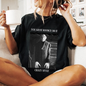 May include: Black t-shirt with a graphic print of a man in a black suit with the text "You must bounce oh it Crazy Style".