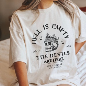 May include: A white t-shirt with a black graphic print that reads "Hell is empty and all the devils are here." The graphic also includes a skull wearing a crown and bats.
