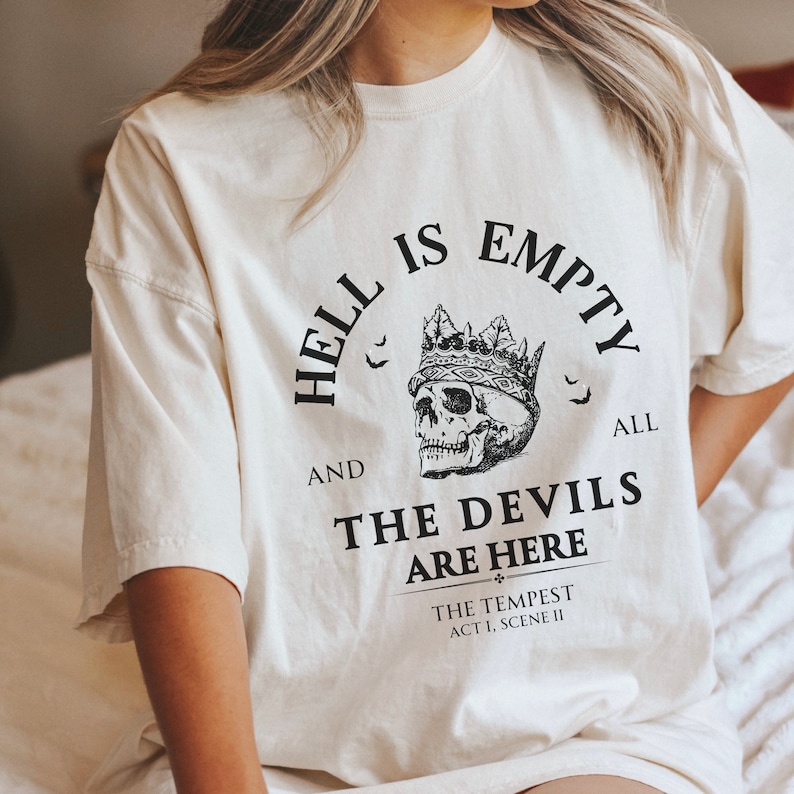 May include: A white t-shirt with a black graphic print that reads "Hell is empty and all the devils are here." The graphic also includes a skull wearing a crown and bats.