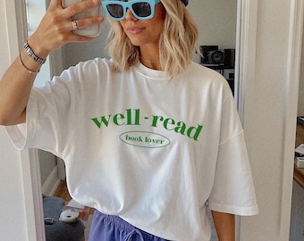 May include: White t-shirt with green text that reads "well-read book lover". The model is wearing a blue beanie and blue sunglasses.