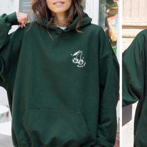 Op de afbeelding: Een donkergroen hoodie met een witte afbeelding van een kers met een nummer 8 erin. De tekst "Lucky you!" staat onder de kers.