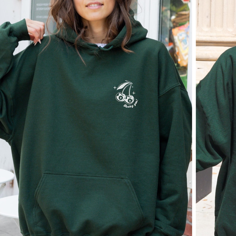 Op de afbeelding: Een donkergroen hoodie met een witte afbeelding van een kers met een nummer 8 erin. De tekst "Lucky you!" staat onder de kers.