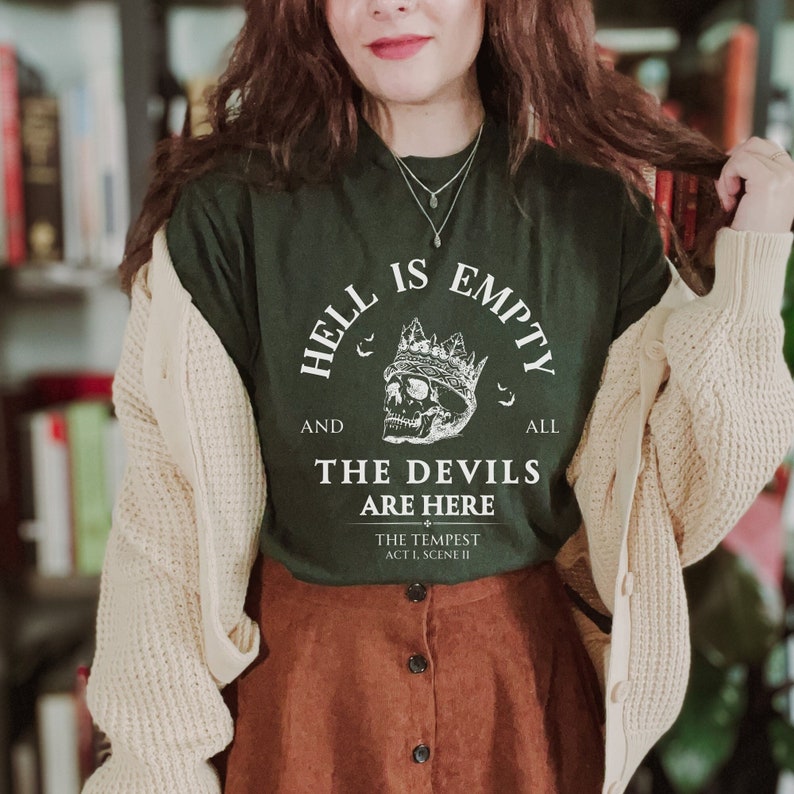May include: A dark green t-shirt with a white graphic print of a skull wearing a crown. The text reads "Hell is empty and all the devils are here" with the quote "The Tempest Act 1, Scene II" below.