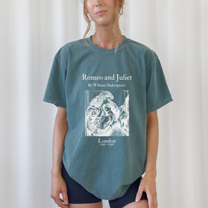 May include: A teal blue t-shirt with a white graphic print of a book cover. The book cover features the title "Romeo and Juliet" by William Shakespeare, a black and white illustration of a couple, and the text "London 1591 - 1596".