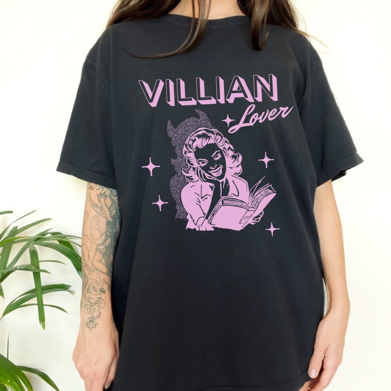 May include: Black t-shirt with a pink graphic of a woman reading a book. The text "VILLIAN Lover" is printed in pink above the graphic.