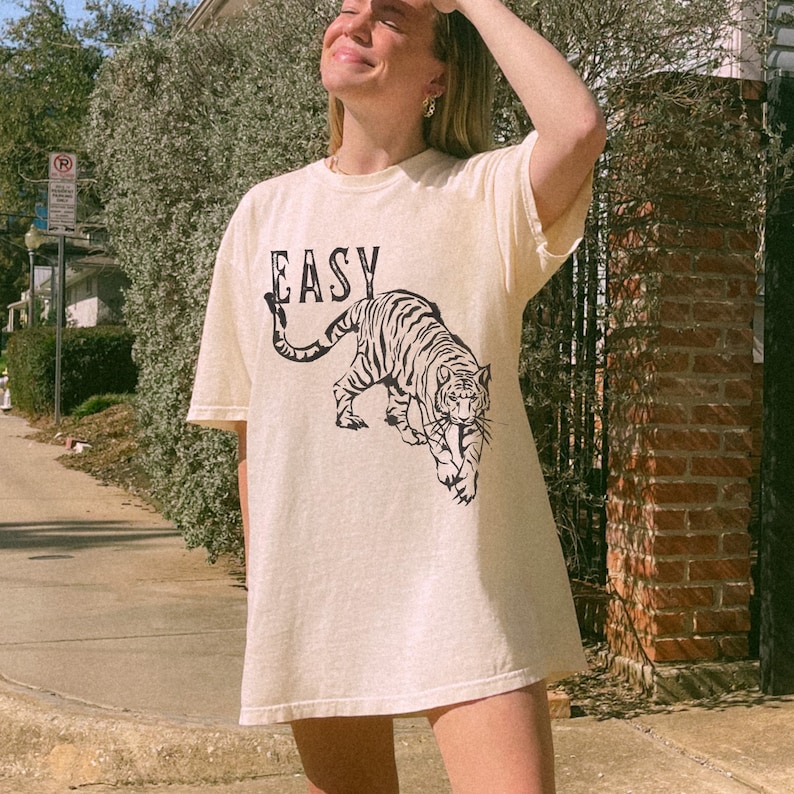 May include: A cream-coloured t-shirt with a black tiger graphic and the word "EASY" printed on the front.