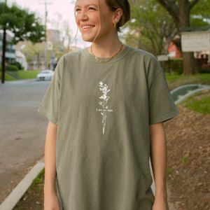 Pode incluir: Uma camiseta verde-s&aacute;lvia com um design floral branco e o texto "I am no man".